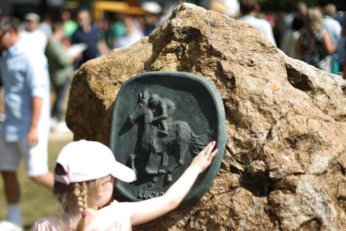Rennbahnbesucher am weissen Stein mit Wappen von Luciano